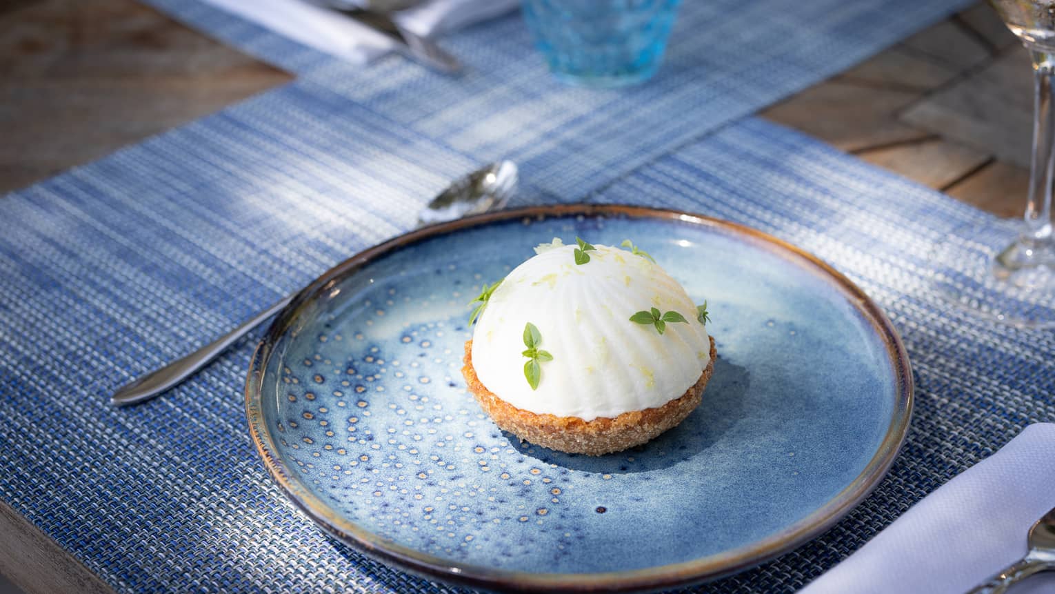 A white dome-shaped tart pastry topped with green leafy garnishes and served on a blue plate