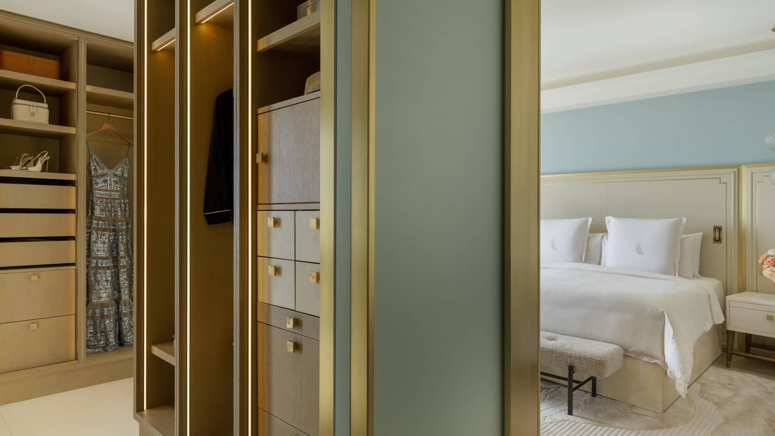 Walk-in closet with built-in shelving and view into luxury king-bedded bedroom