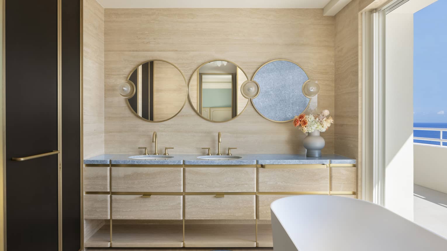 Modern hotel suite bathroom with circular mirrors, freestanding tub and walk-out, sea-view balcony