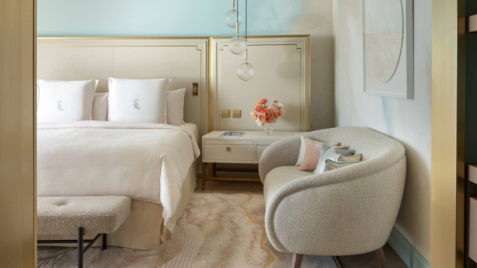 Elegant hotel suite bedroom with king bed, modern two-seat sofa, hanging glass pendant lights and turquoise wall