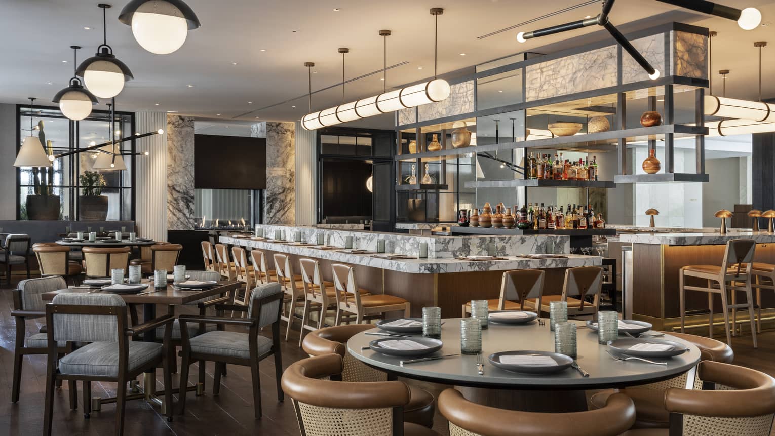 The interior of a well lit restaurant with wood and grey accents and a large bar area.