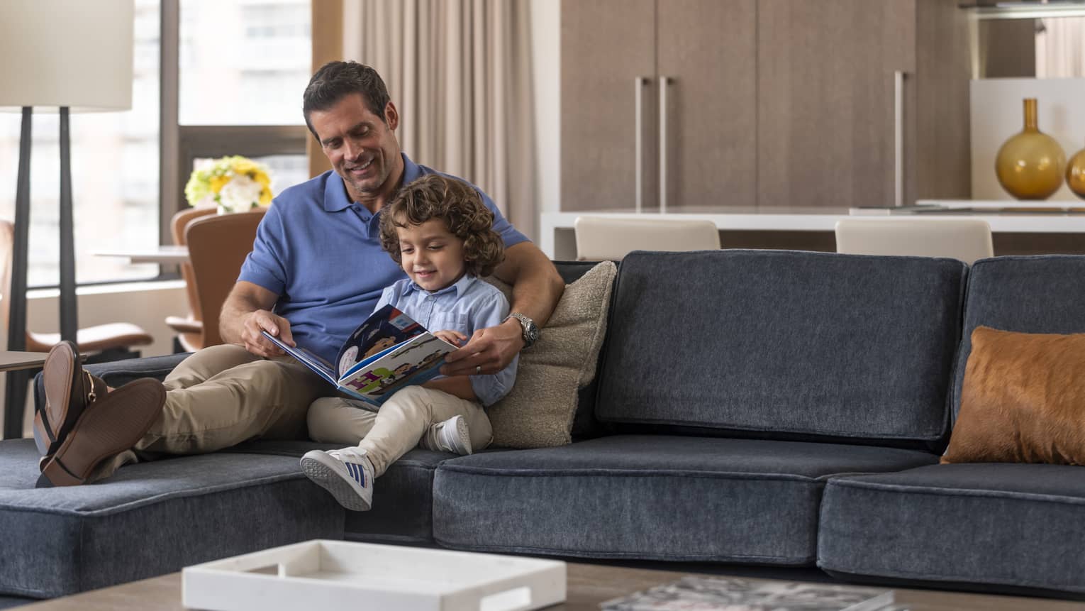 Man sits on a sofa with young boy reading book