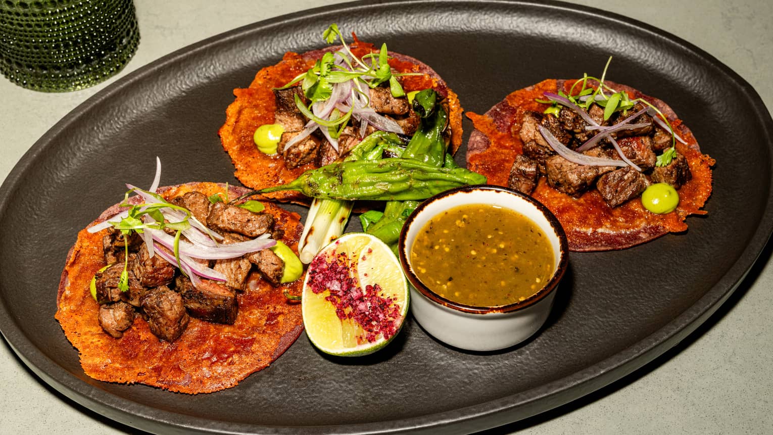 A black oval platter holds colourful food items, garnishes and a small bowl of sauce.