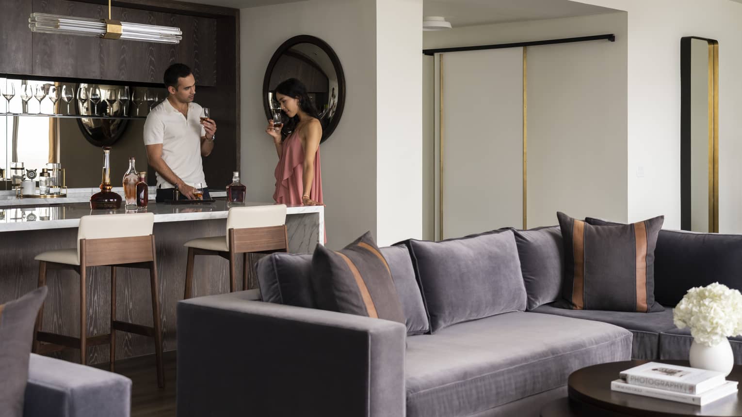 A man and woman in a large hotel room drinking wine.