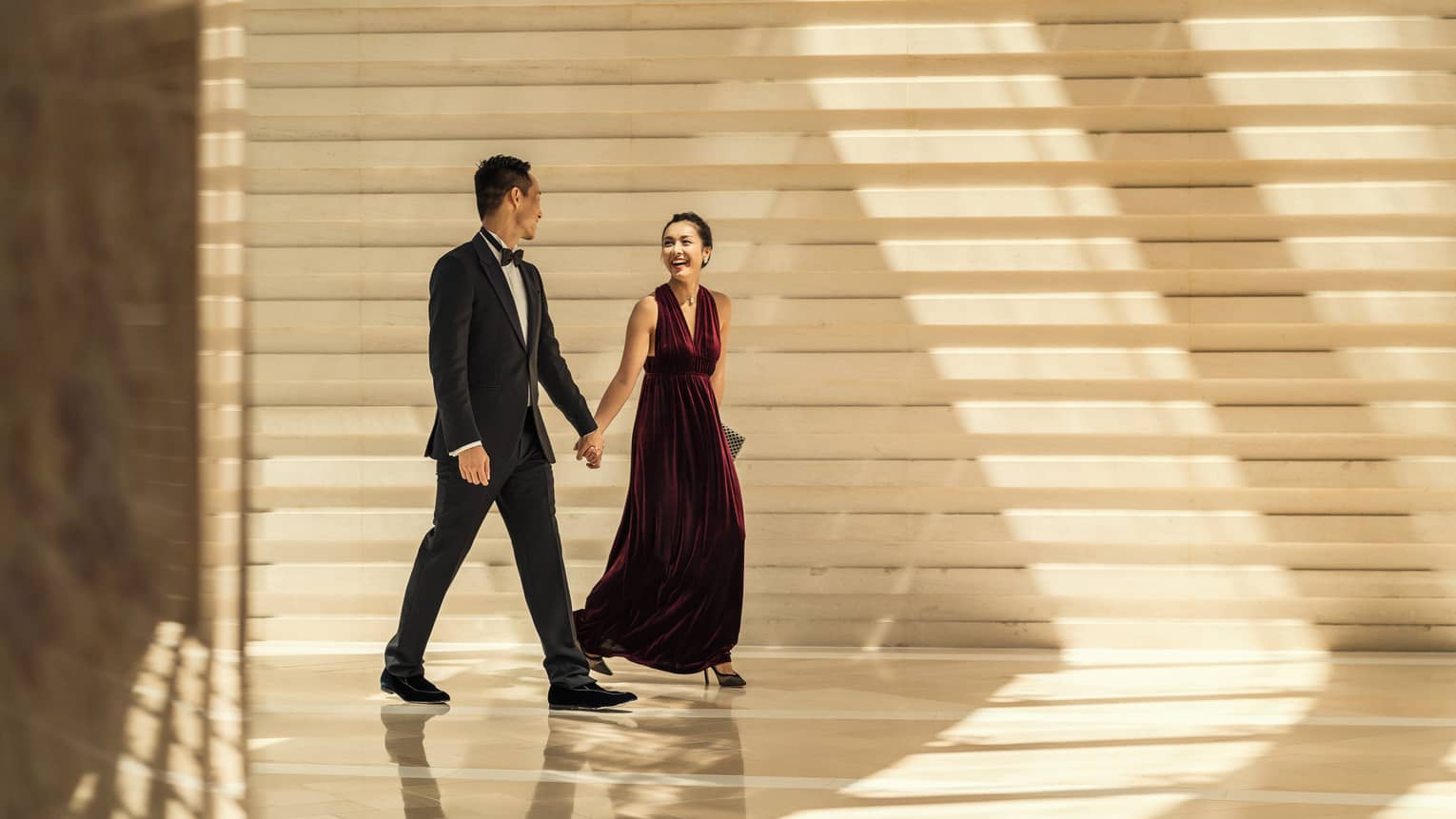 Man and woman in formal wear hold hands at Four Seasons Hotel Hong Kong.