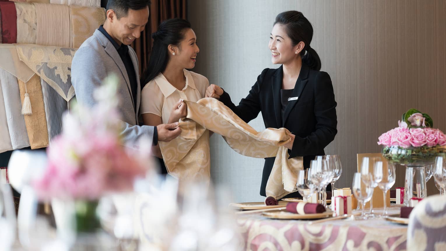 Hotel staff stand by a beautifully set table with flowers and glassware, discussing banquet linen. One explains to others, who smile and engage in conversation