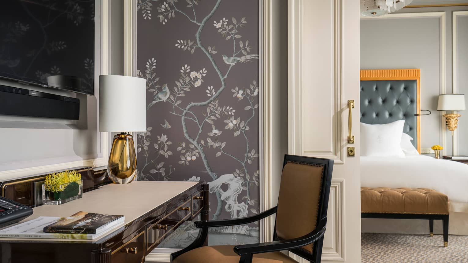 Black desk with orange glass lamp with white shade, wall panel with lilac tone images of trees, birds 