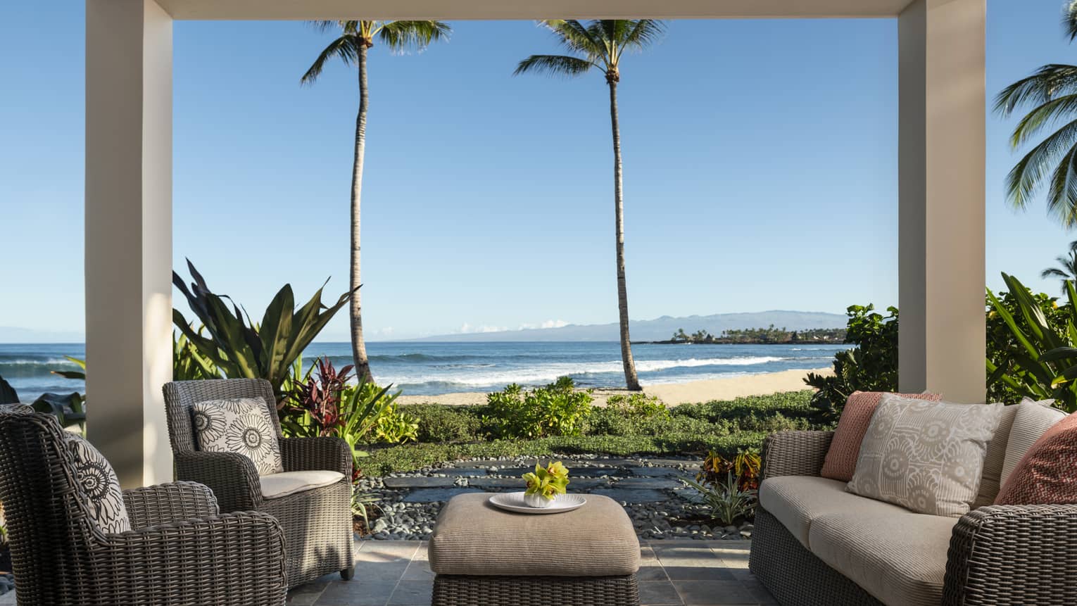 Covered lanai with dark wicker sofa and two matching arm chairs, ottoman, beach view