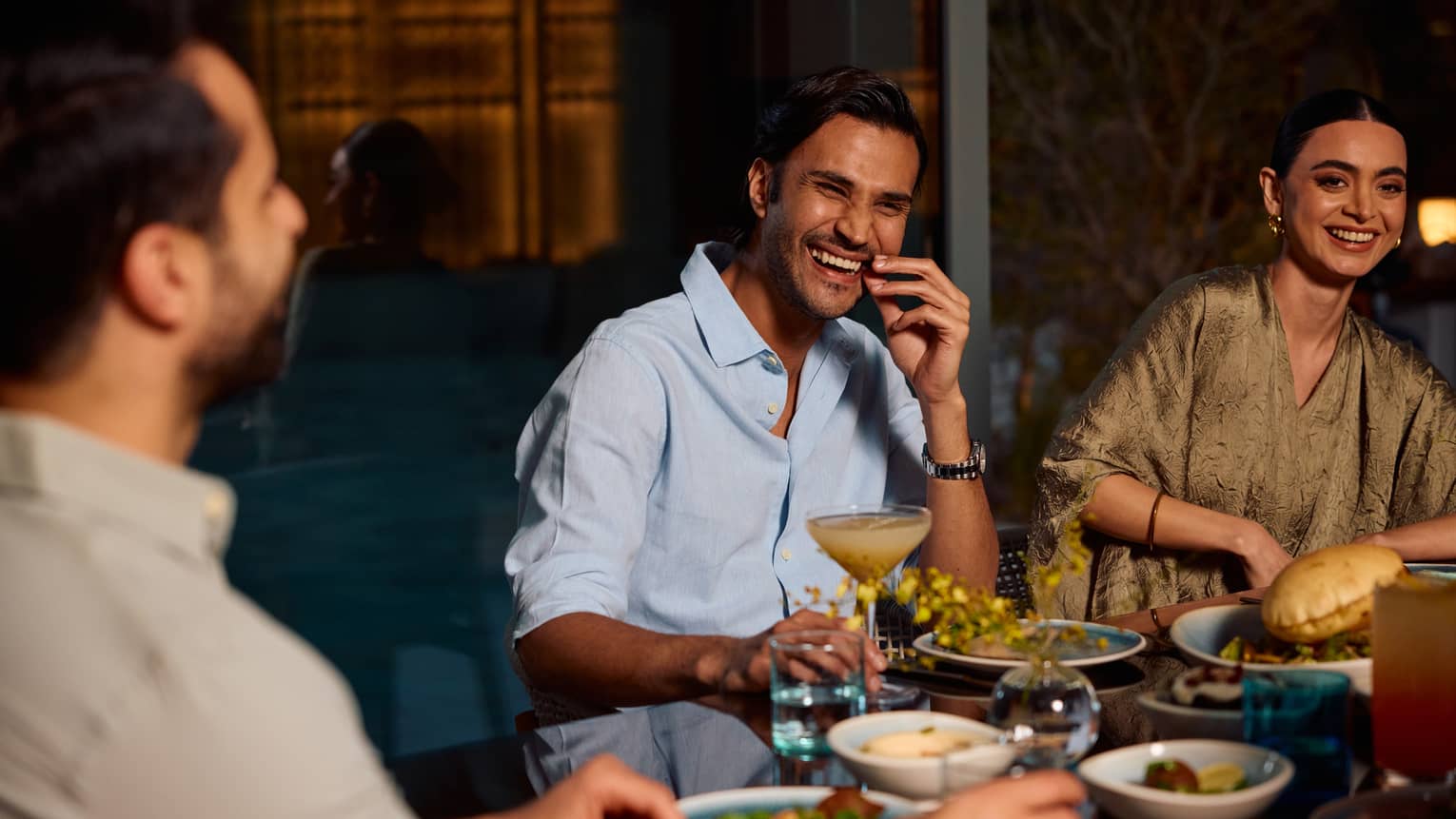 Three people sit smiling around a dining table