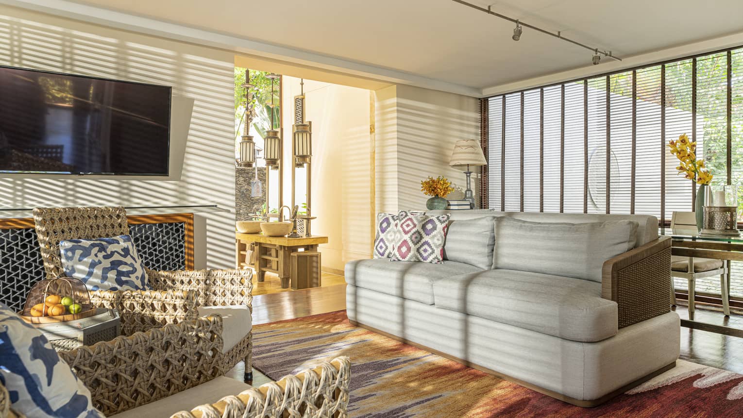 The sun streams into a living room through wooden window shutters