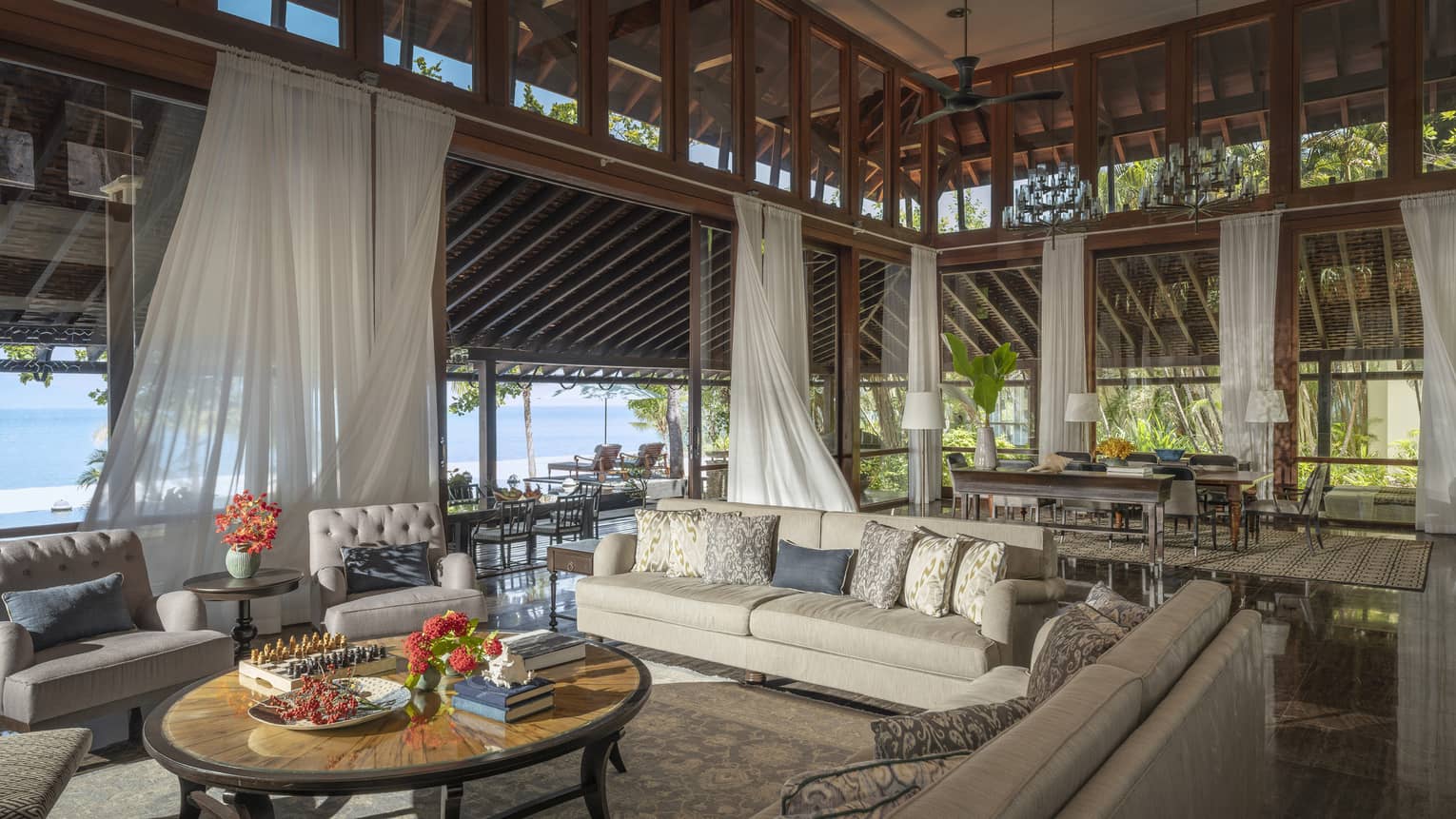 Vast indoor-outdoor living room and great room with high ceilings, flowing white curtains, beach view