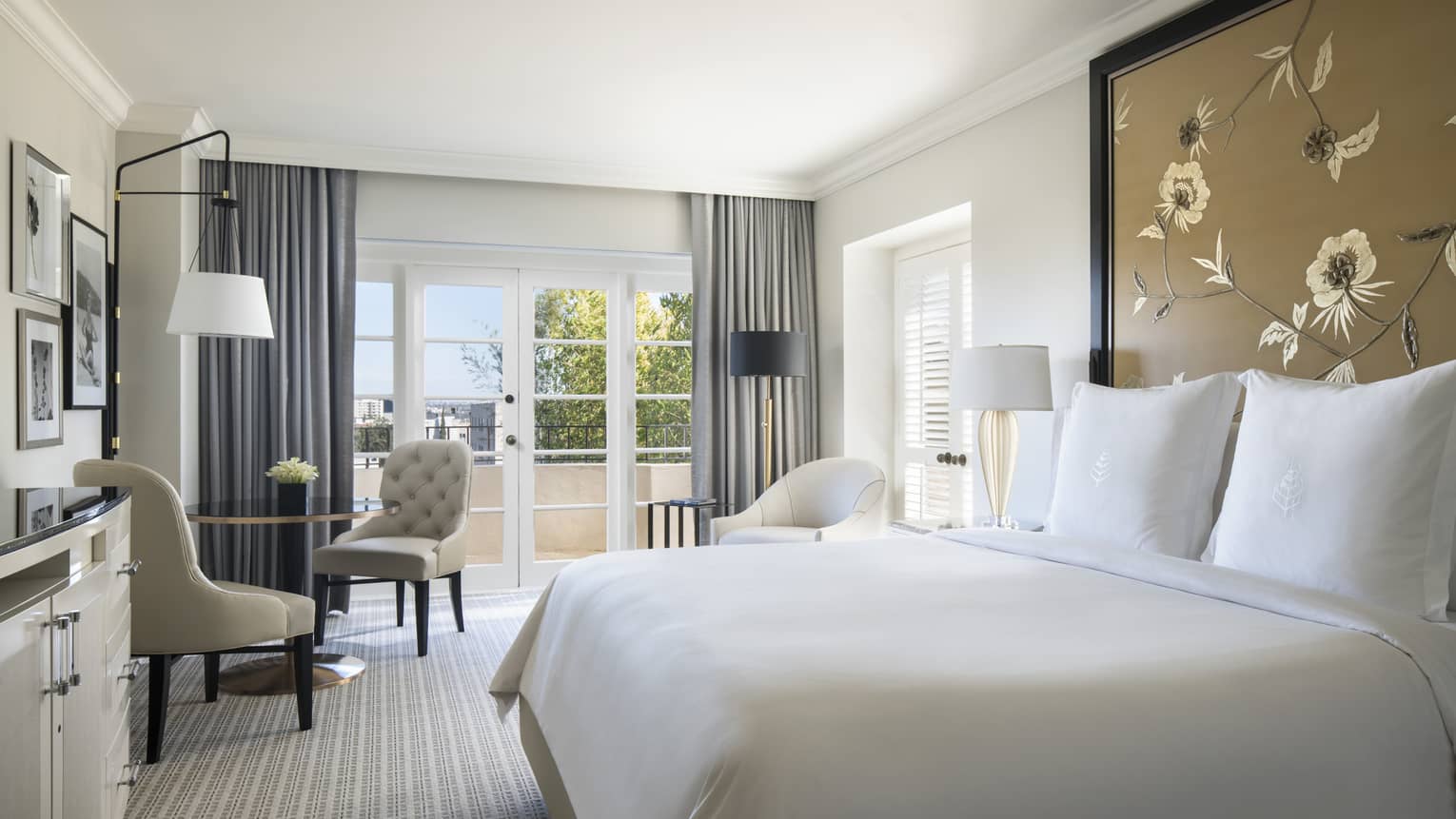 Premier Balcony Room bed with white linens against tall floral headboard, cafe table by balcony doors