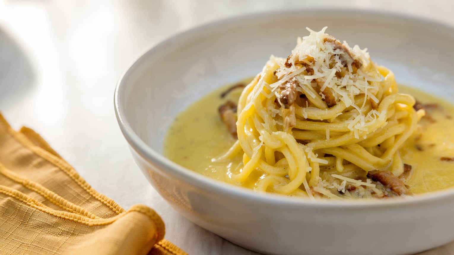 Eggs and noodles in a bowl with a yellow napkin beside it.