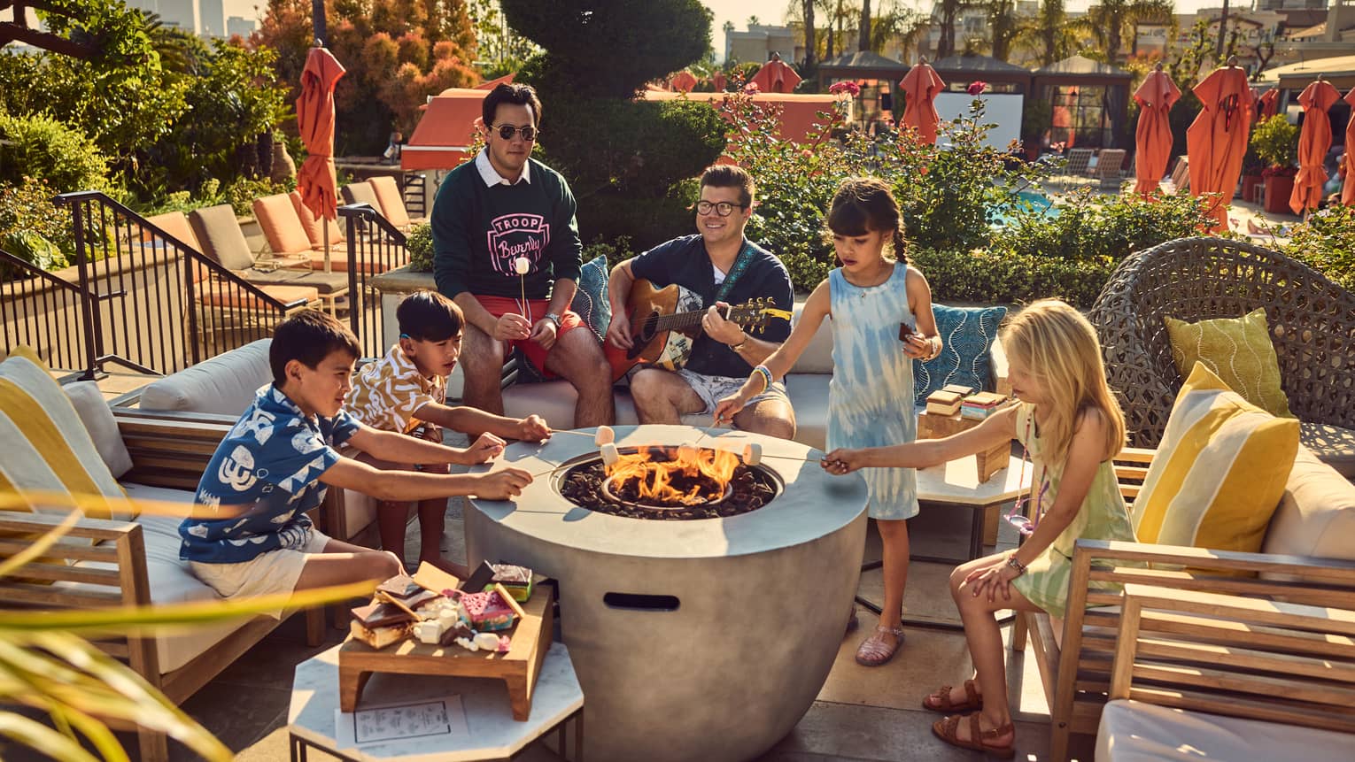 Young guests roasting marshmallows by a fire pit while a person plays the guitar