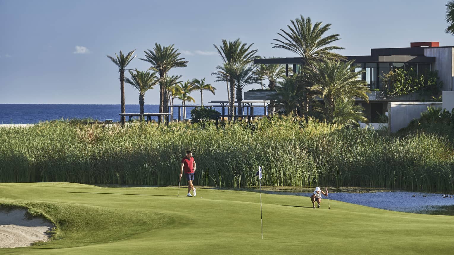 Two golfers enjoy a day on the golf course at four seasons Los Cabos with palm trees and the ocean in the background