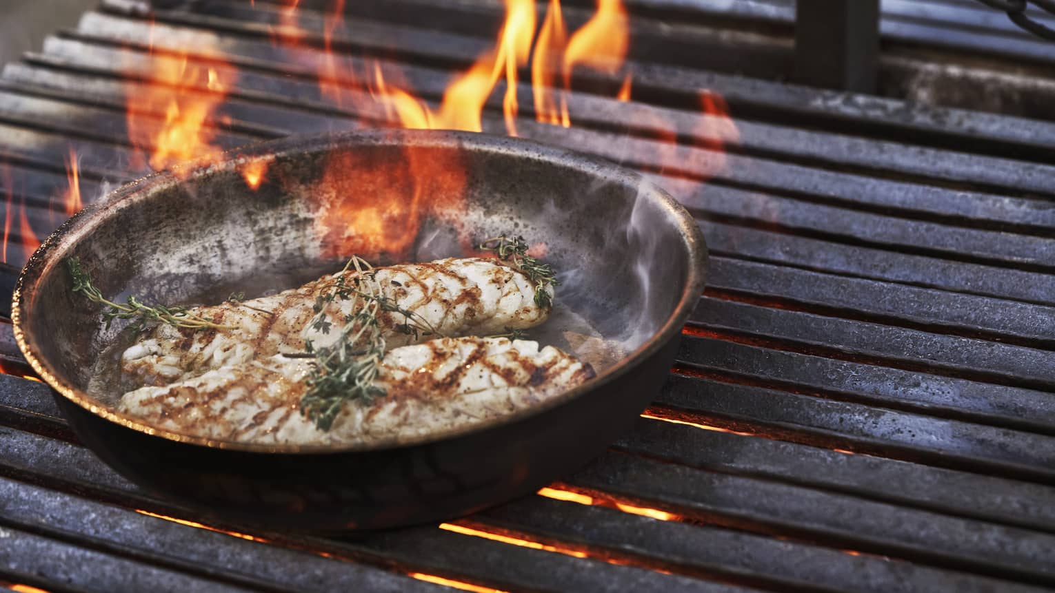 Meat cooking on a fire grill in a round and flat pan.