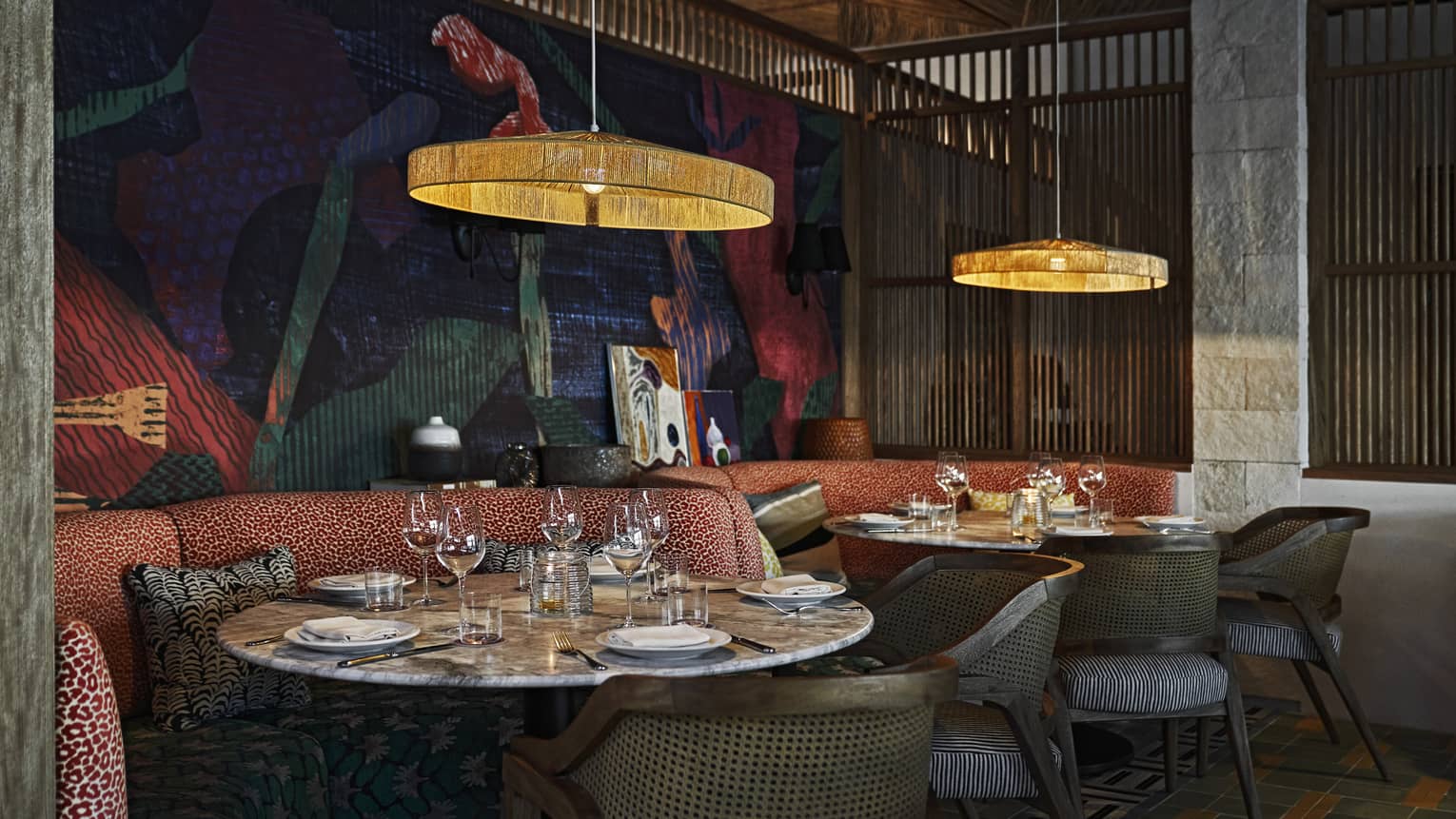 An intimate indoor dining space with elegant lighting, upholstered booth and chair seating, round tables and artistic decor