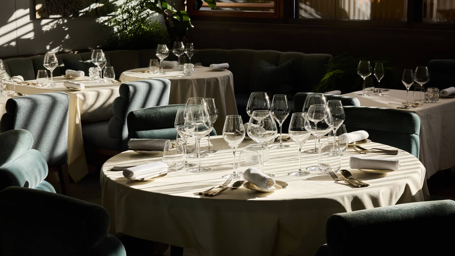 An indoor dining space with dramatic daylight filtering through window blinds and featuring tables, chairs, and place settings for a meal