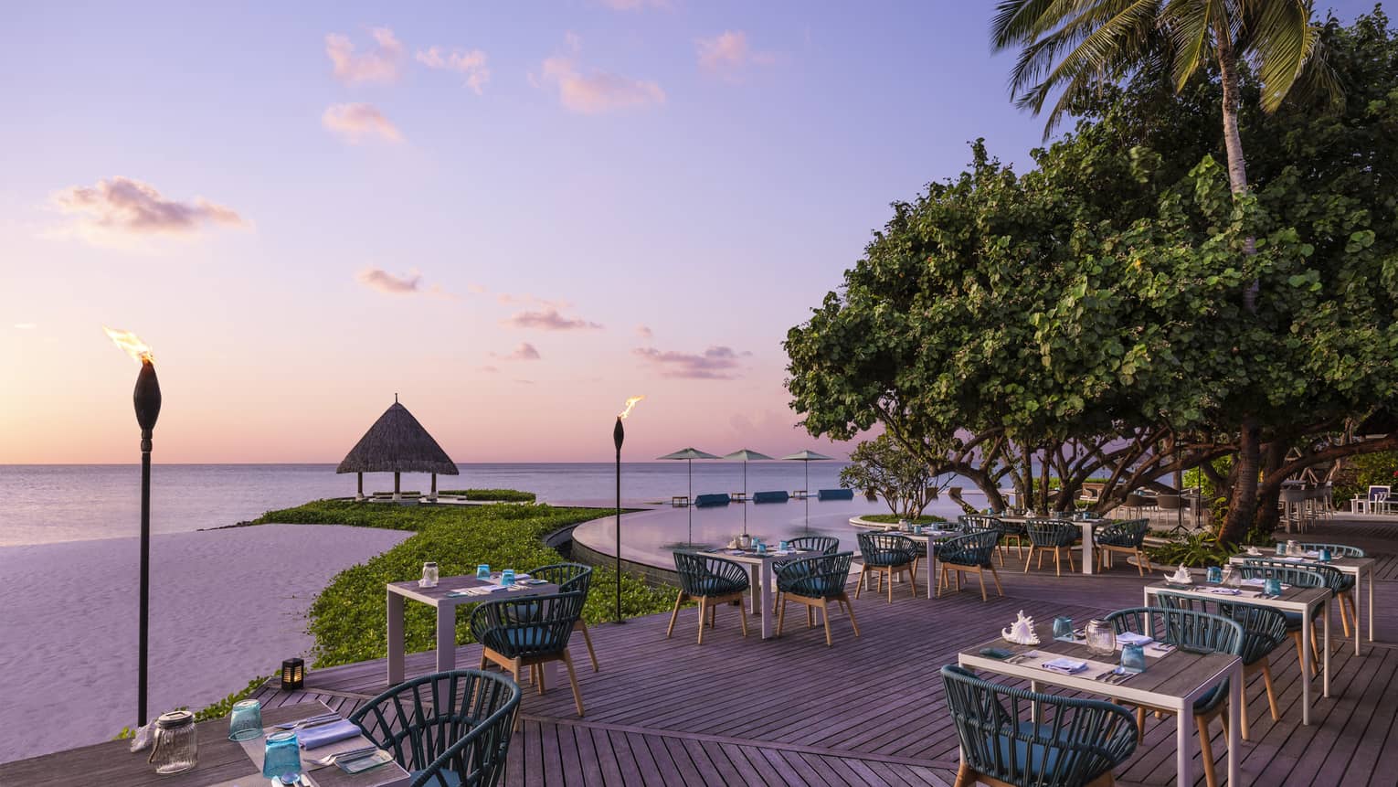 Tiki torches line the oceanside Reef Club terrace that's ready for guests with tables set with plates, silverware, blue napkins, all overlooking the ocean
