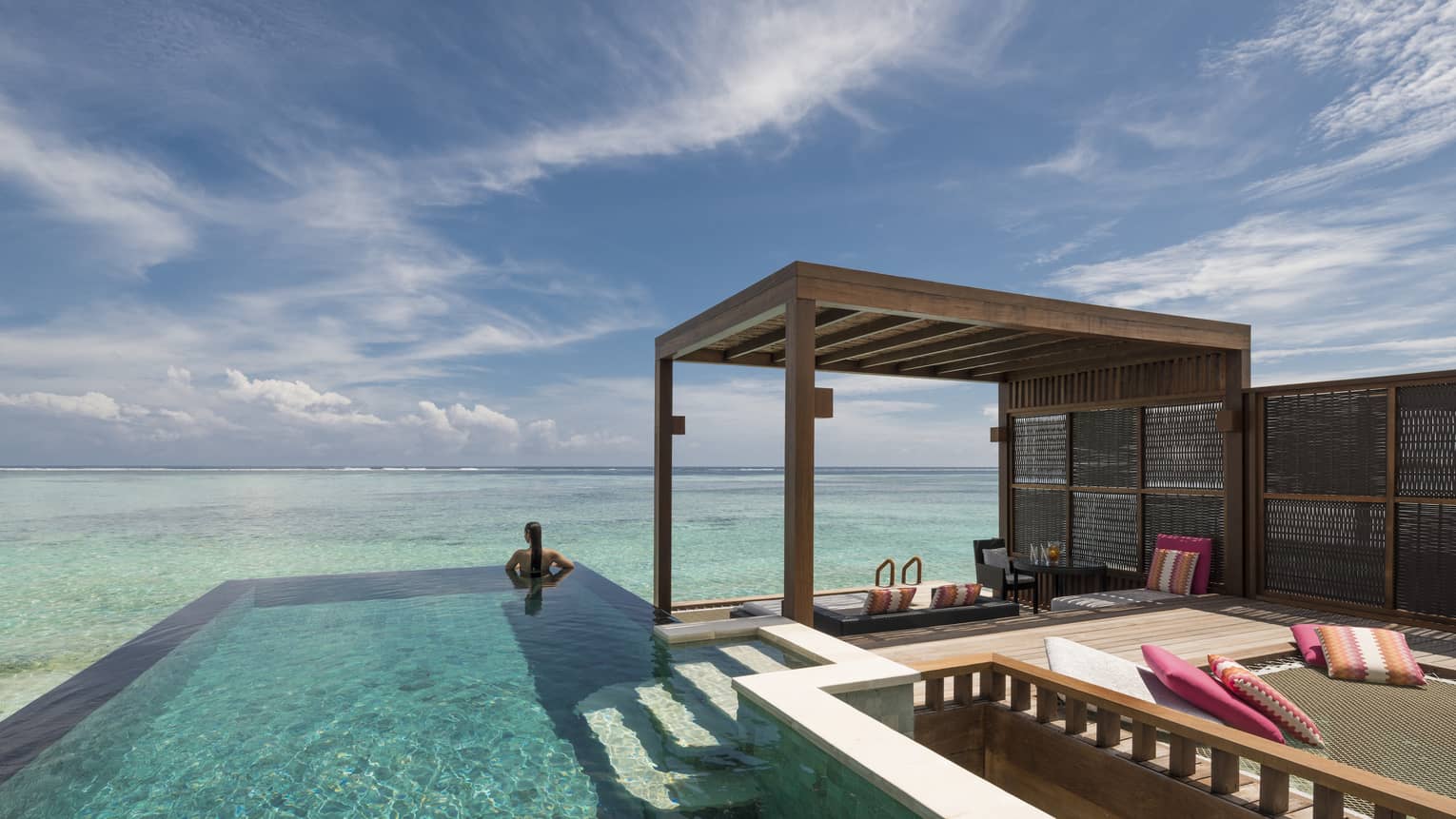 Woman looks out at ocean from private pool on sunny patio of sunset water villa