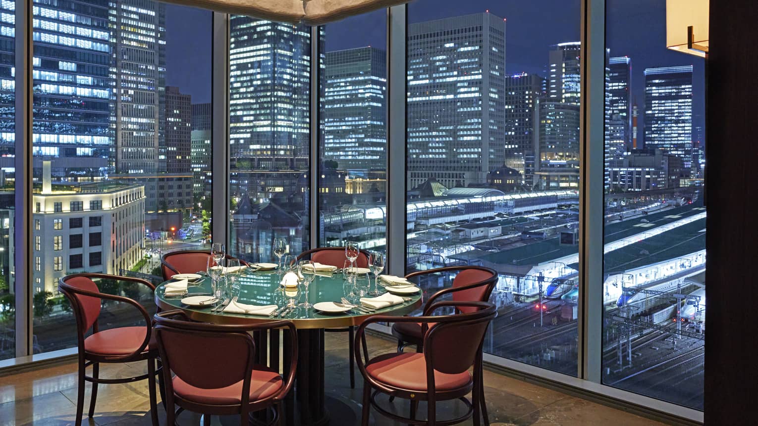 A round table and six chairs at Maison Marunouchi, floor-to-ceiling windows with views of downtown Tokyo at night