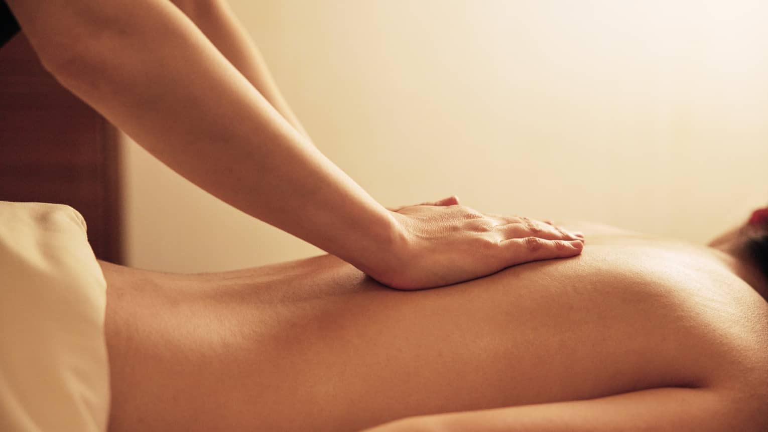 Masseuse rests hands on woman's bare back as she lays on massage table