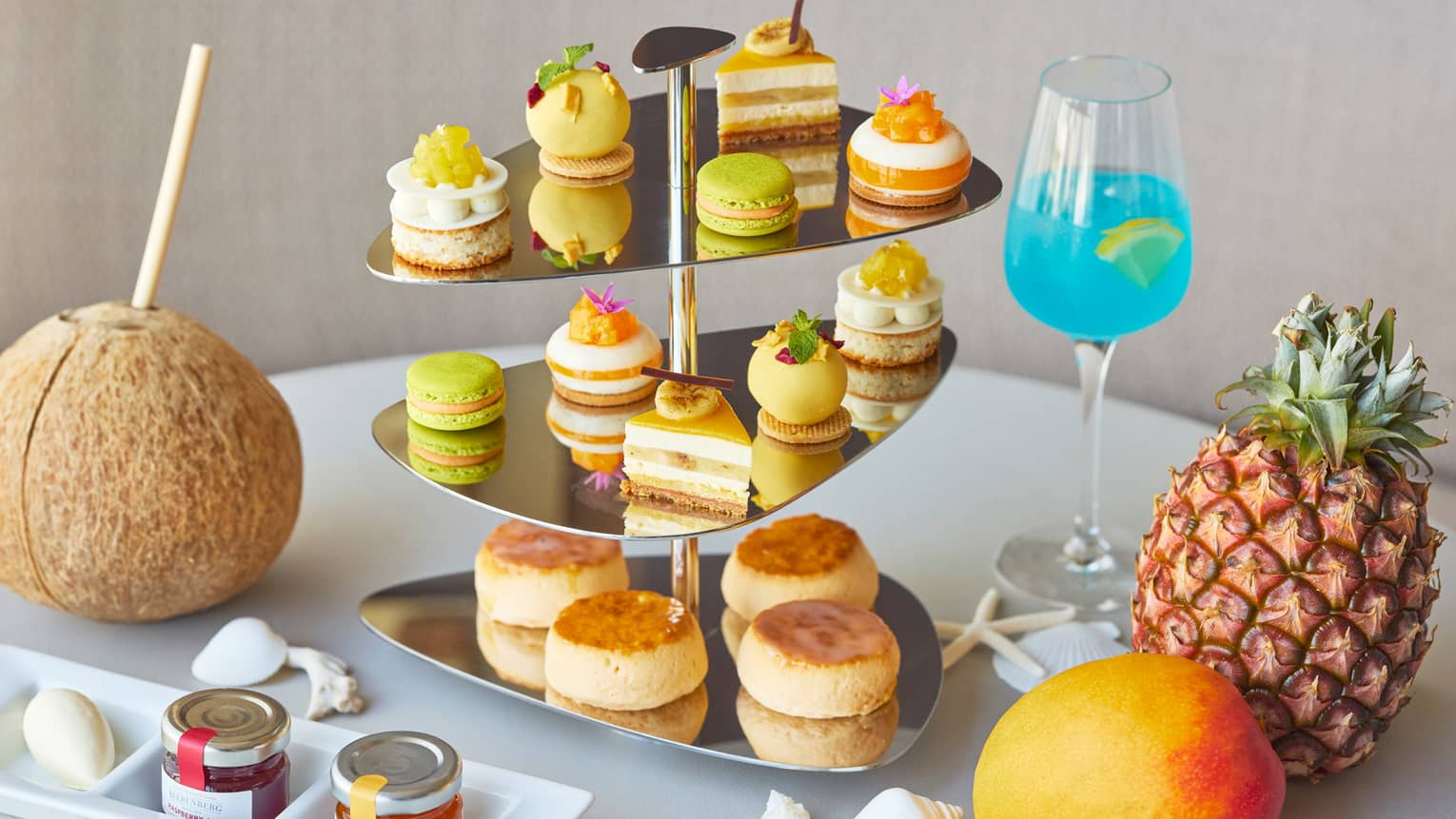 Tropical Afternoon Tea display with sweets and savouries on metal stand, whole mango, pineapple and coconut garnish