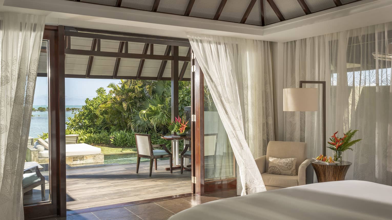 Bedroom with sheer curtains, opened doors to wooden deck and beach view
