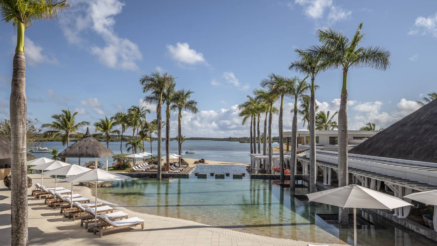 Wading pool with rows of lounge chairs and white umbrellas, flanked by palm trees