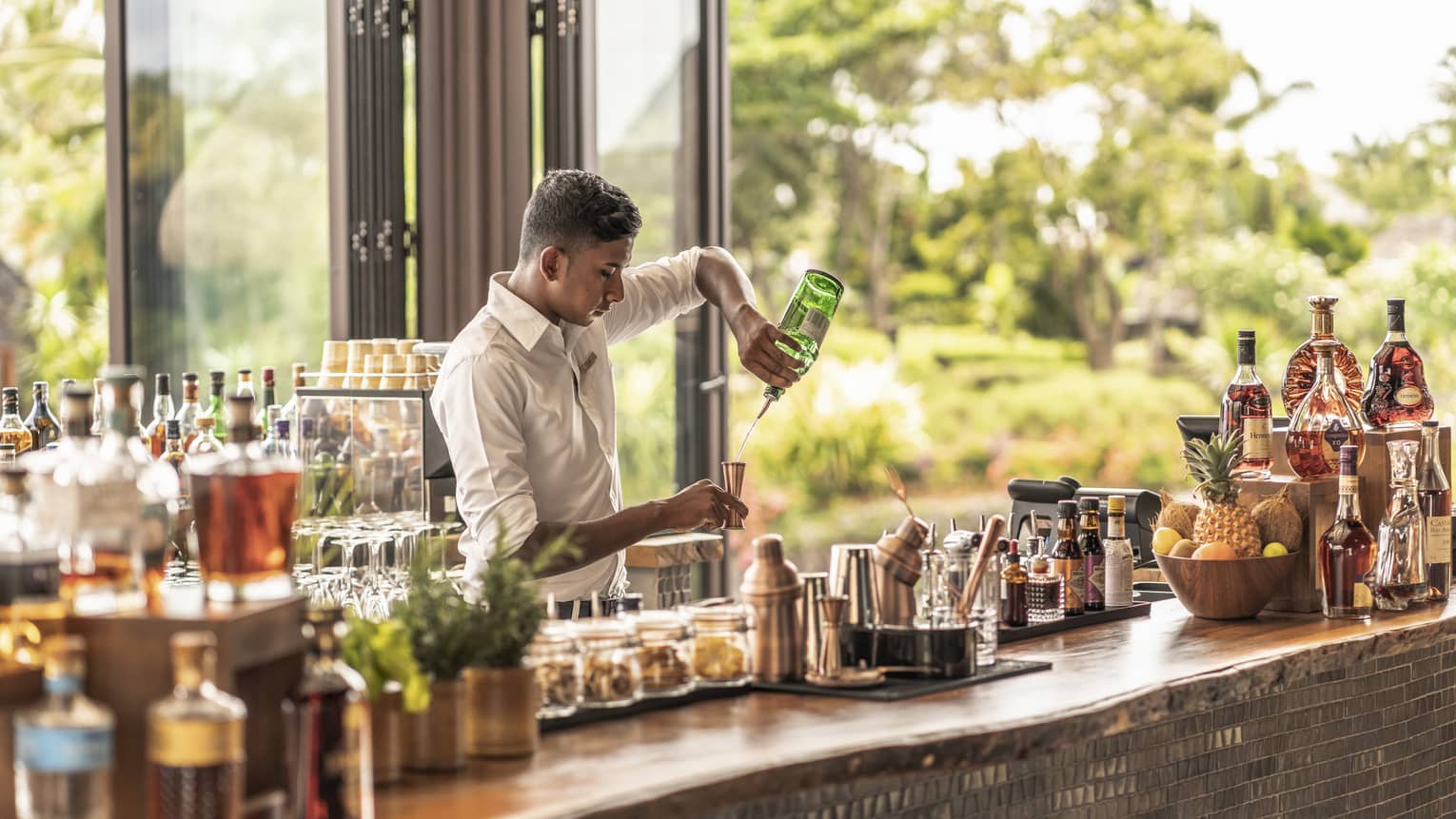 Bartender behind stocked bar pouring gin into a copper jigger