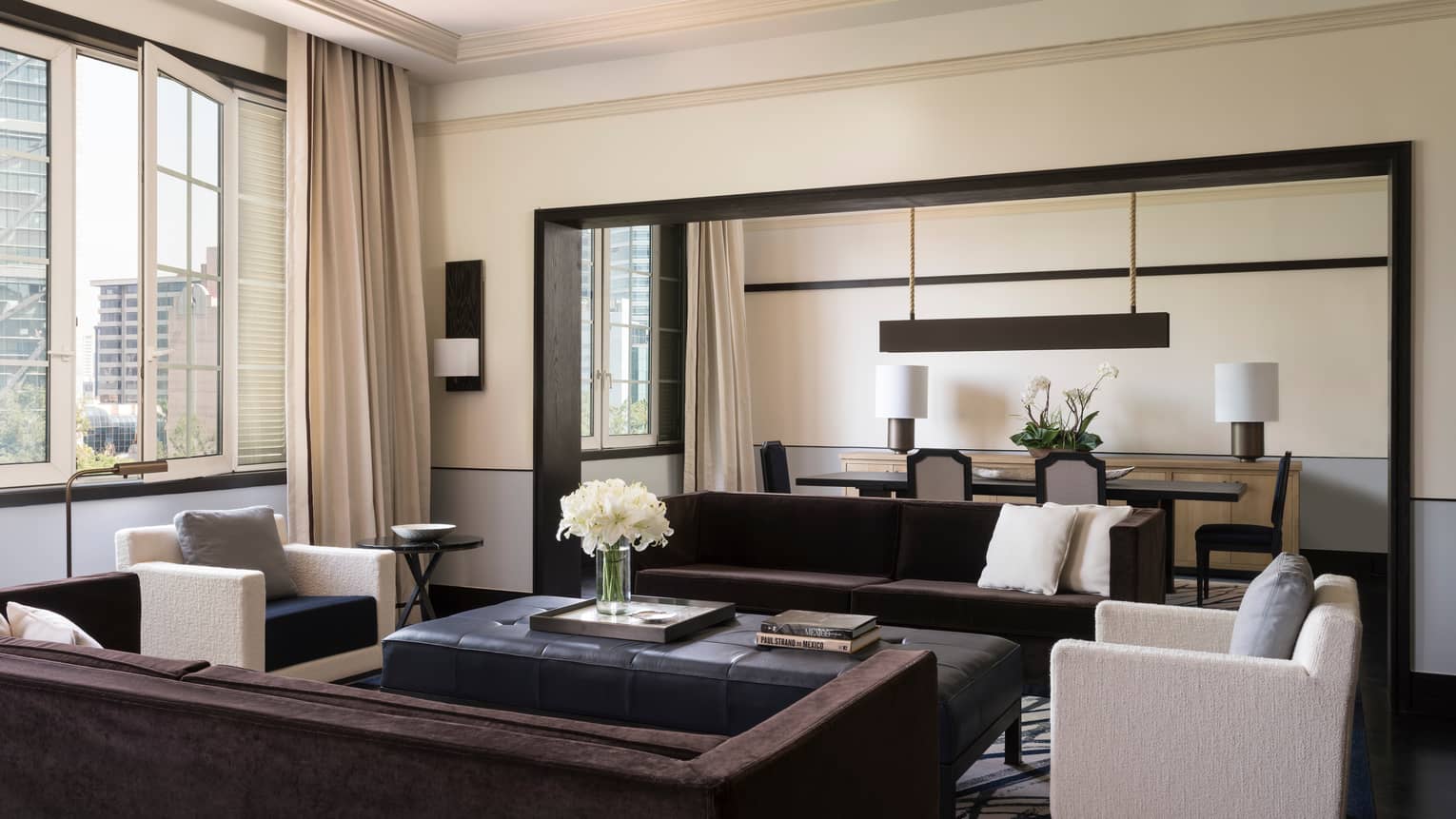 Presidential Suite bright living room with long sofas, white armchairs, tall sunny window, dining room
