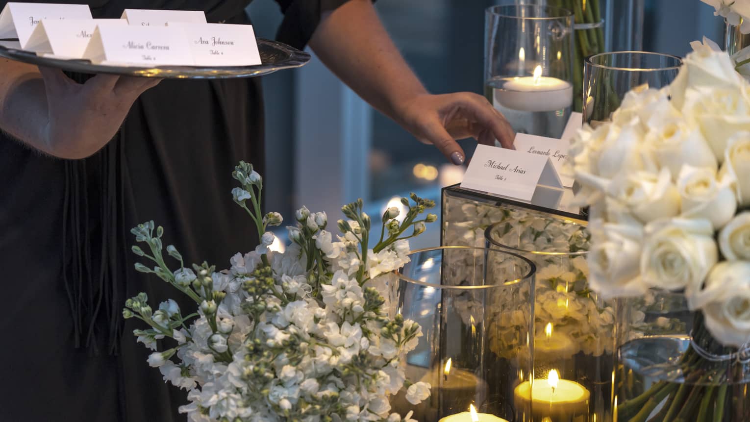 Event staff with tray places name cards on elegant banquet table with white flowers, candles
