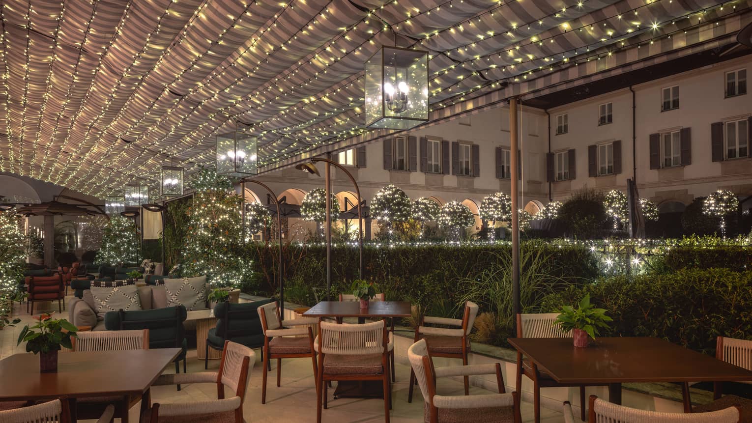 An outdoor dining area with holiday decor, including strings of holiday lights overhead