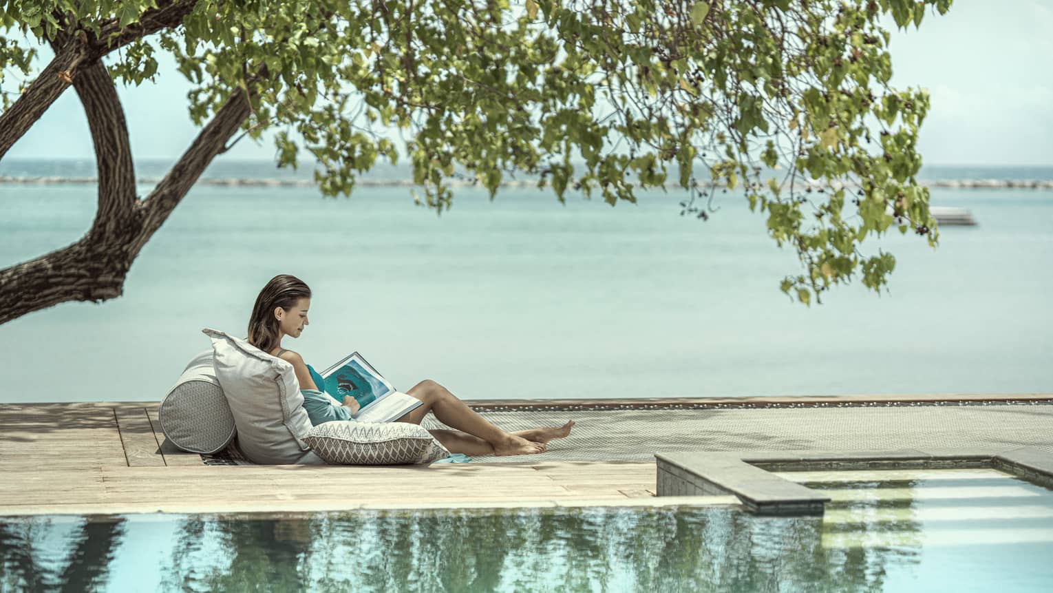 Woman reading next to pool, ocean view
