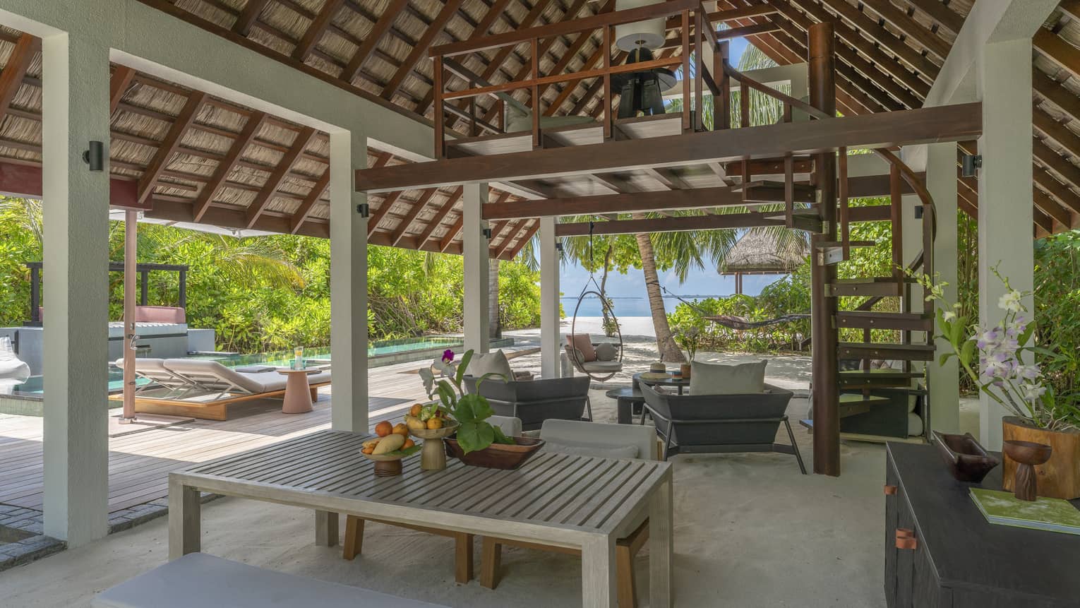 Dining and lounge area under a vaulted outdoor pavilion, next to a pool