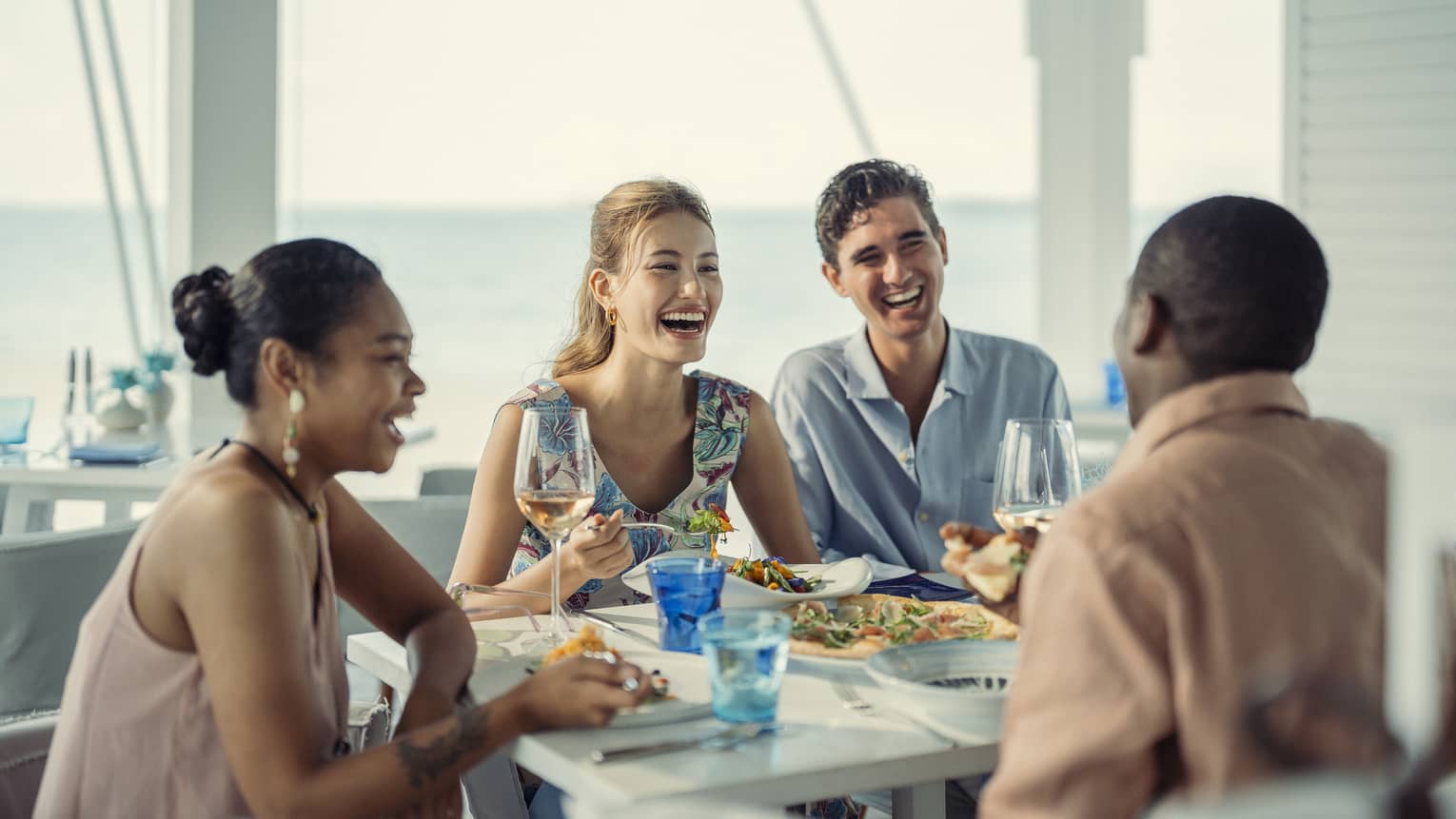 Two couples laugh as they share a meal at Blu Beach Club