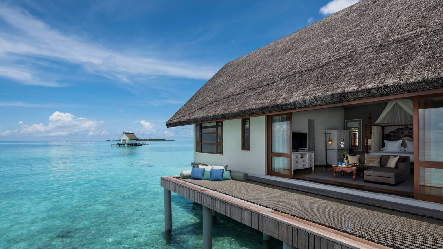 Overwater bungalow with thatched roof, set atop clear turquoise water