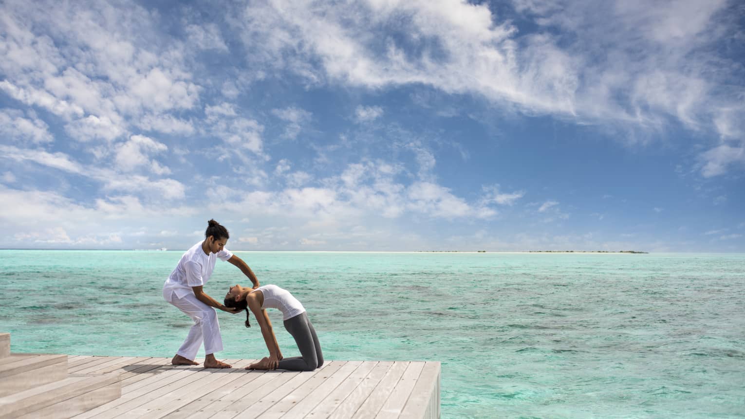 Woman leans back into hands of Yoga Therapist on dock over lagoon