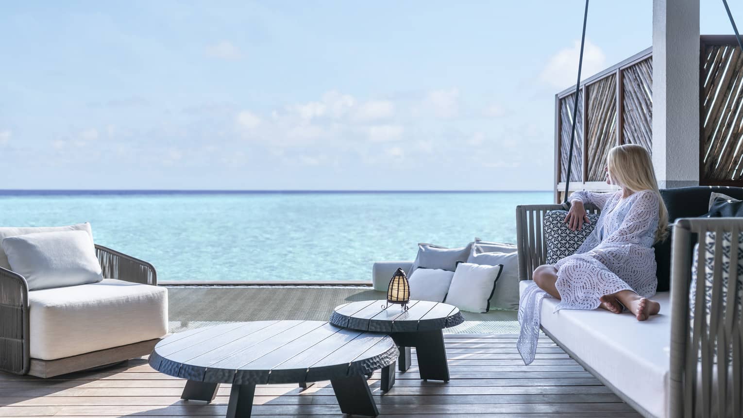A guest relaxes on a swinging bench on a patio overlooking the ocean