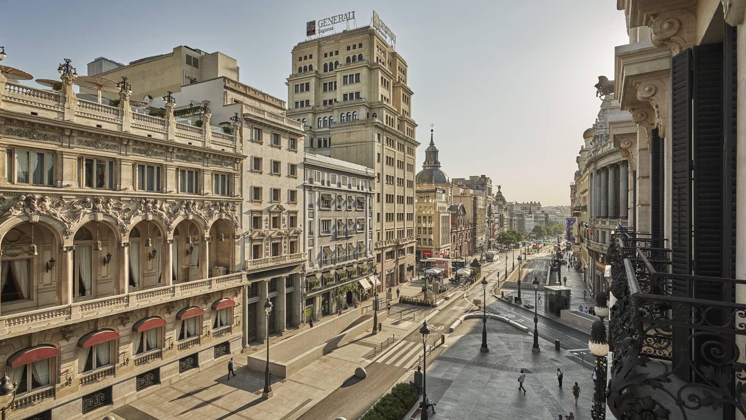 Street view from a Juliet balcony with historic buildings, arched windows and a mix of architectural styles lining a broad avenue on a clear day