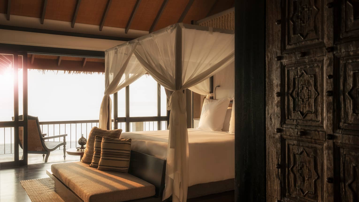 Mezzanine Suites cushioned bench with pillow at foot of canopy bed with white curtains in sunlight