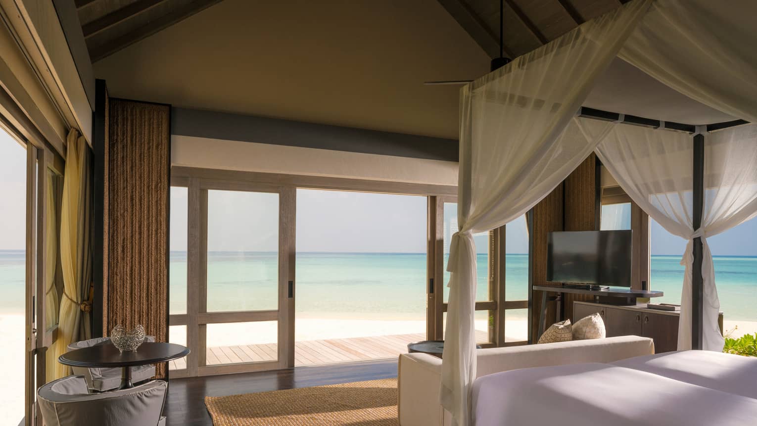Beach Villa bedroom with white canopy bed by sliding doors to patio, lagoon views