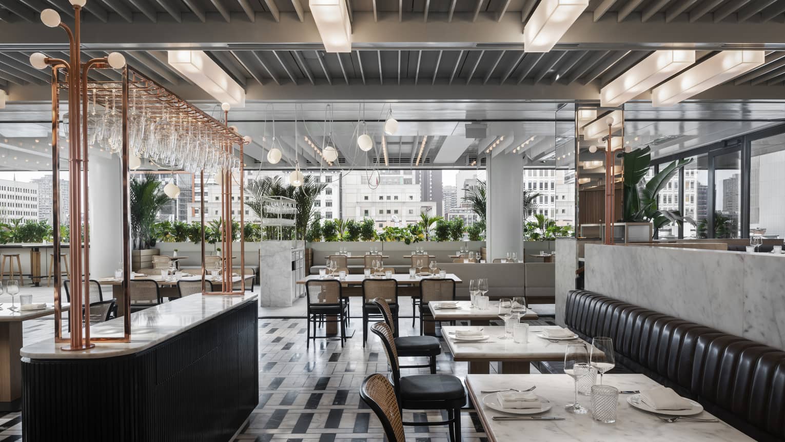 Restaurant with black bar and leather booths, white marble tables, black-and-white tiled floors, opening to terrace