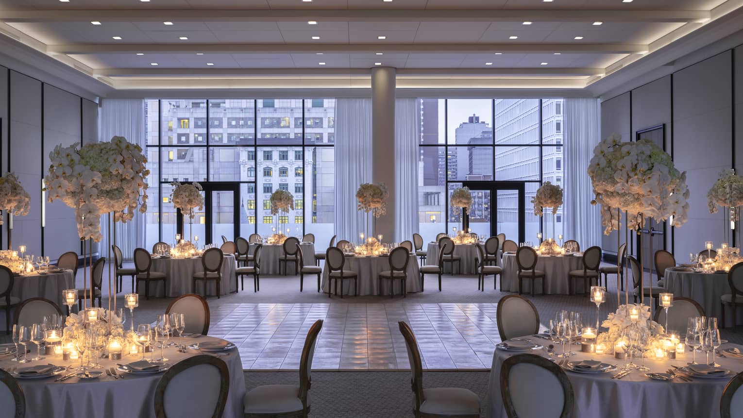 Palais des Possibles Ballroom with floor-to-ceiling windows, round tables with candles and large floral displays