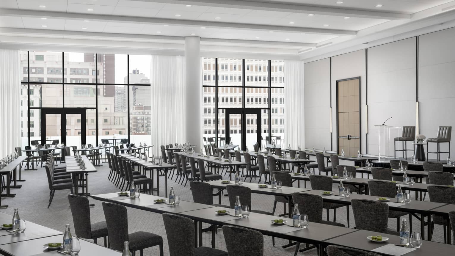 Rows of black tables set with green macaroons, water facing podium in light-filled ballroom