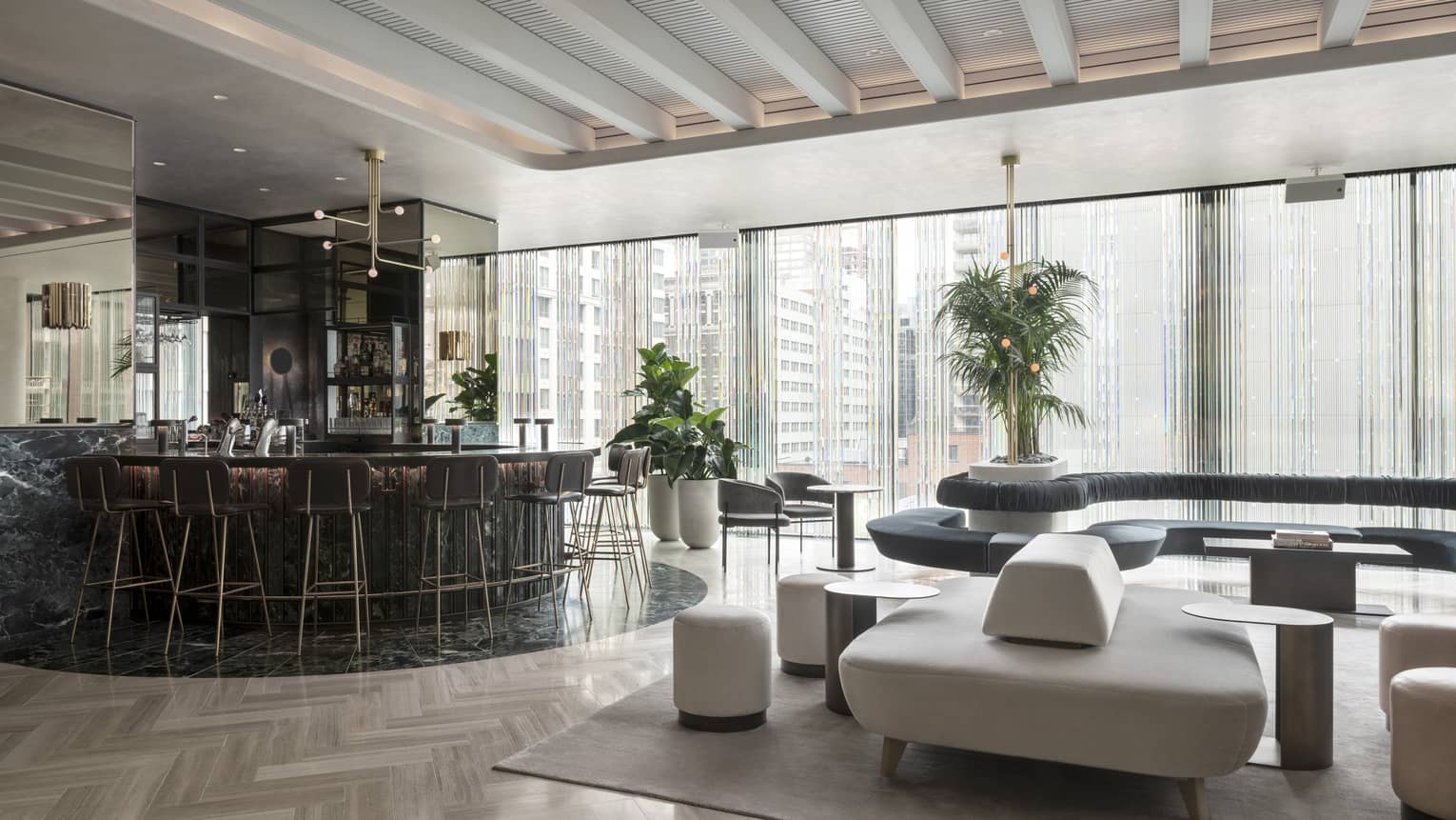 A curved black marble bar, modern grey and black furniture and a wall of windows sit beneath tall beamed ceilings at MARCUS Day Bar