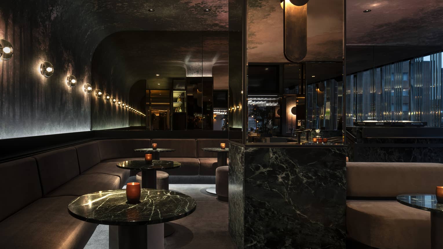 Dimly lit MARCUS Bar features rounded mauve banquets and black marble cocktail tables