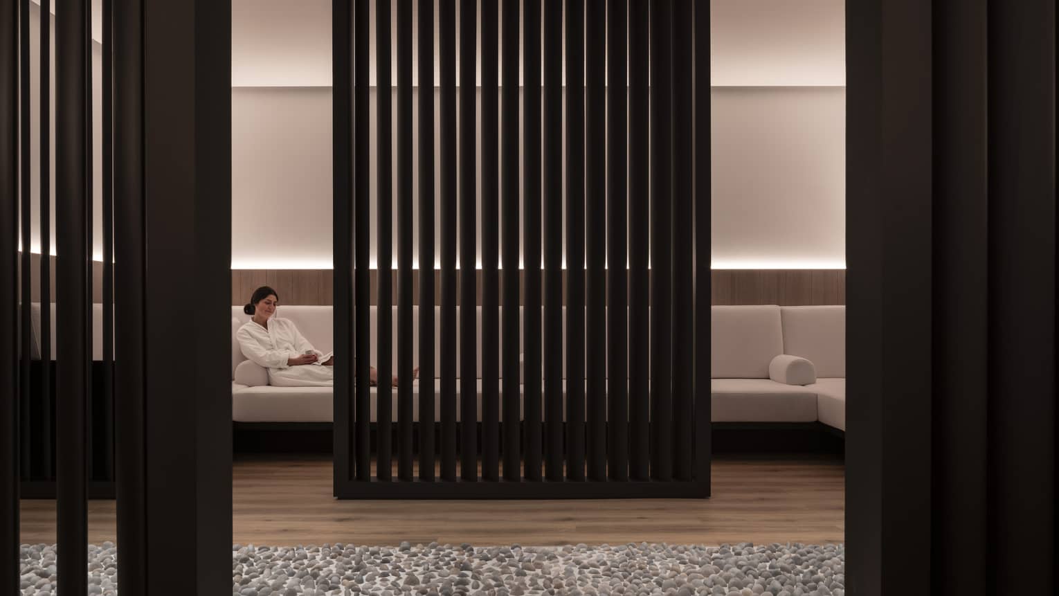 A woman lounges on a large white couch obscured by a black privacy wall. 