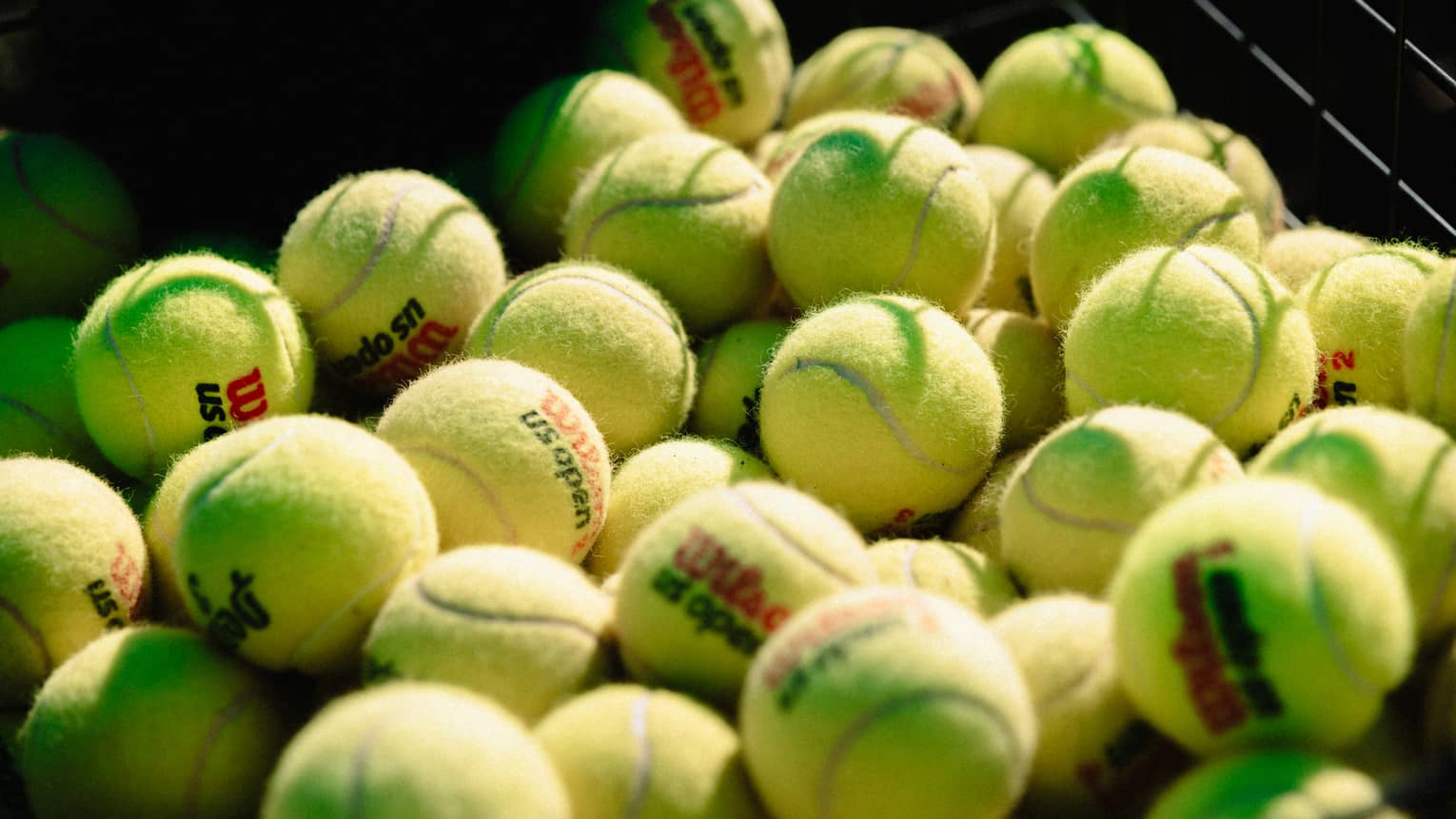 Collection of tennis balls stacked up near a net