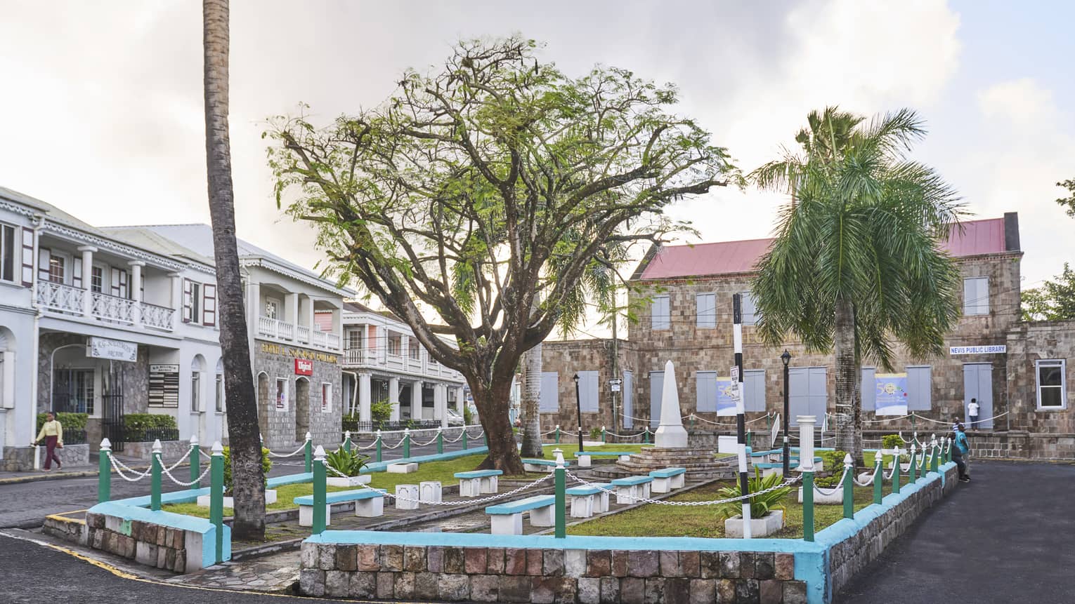 A small outdoor sitting area on a street with benches, grass and trees.